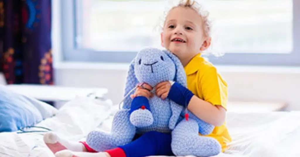 Boy wearing yellow shirt is cuddling with a blue bunny
