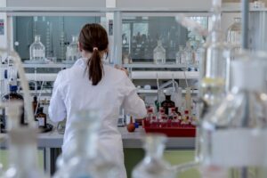 Woman standing in a research lab wearing a white coat with her back to the camera.