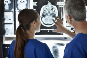 Two doctors, a man and a woman, in blue scrubs look at a brain scan.