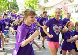 Ella and her mother running among friends all wearing purple shirts at Ella's Race in 2019