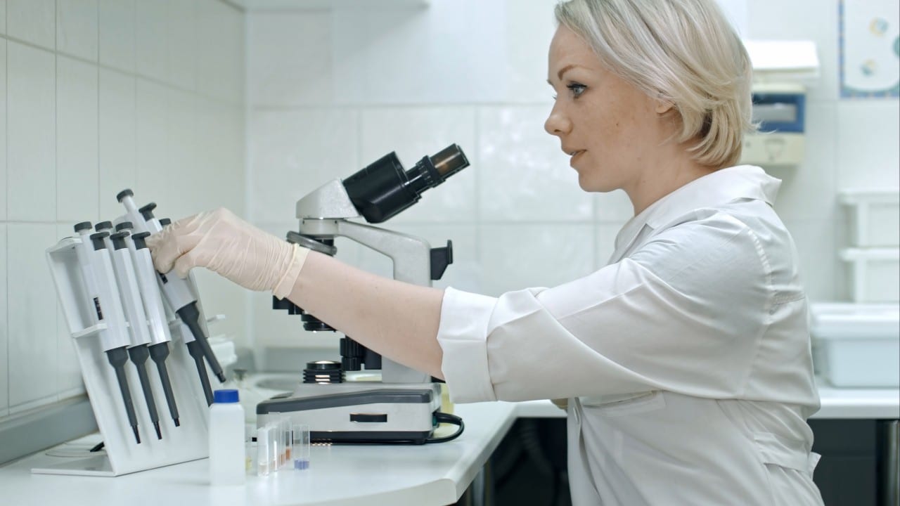 A blonde woman in a lab coat is conducting genetic research in the lab.