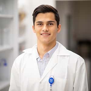 Nathan Bliss is dressed in a white lab coat standing in a research facility.
