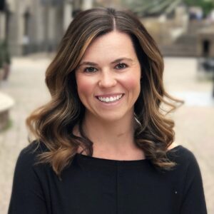 Kristen Harrison stands in a lovely town square with her arms folded wearing a long-sleeved black shirt.