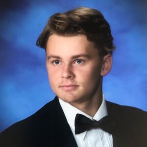 Logan Drew's senior picture, in which he is wearing a suit and bowtie in front of a blue background.