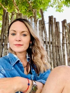 Lindsay Sledge sits in front of a pretty wooden fence on a sunny day.