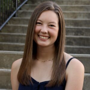 Madison Lee Intemann poses for a picture, sitting in front of concrete stairs and smiling.