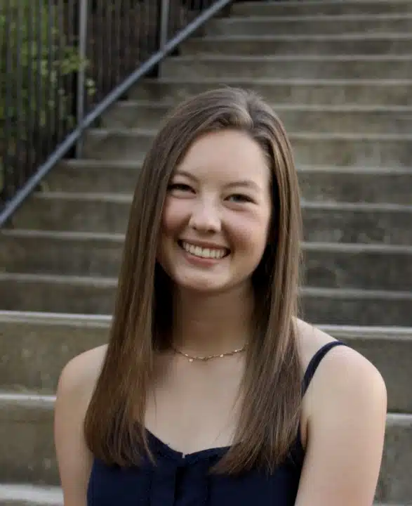 Madison Lee Intemann poses for a picture, sitting in front of concrete stairs and smiling.