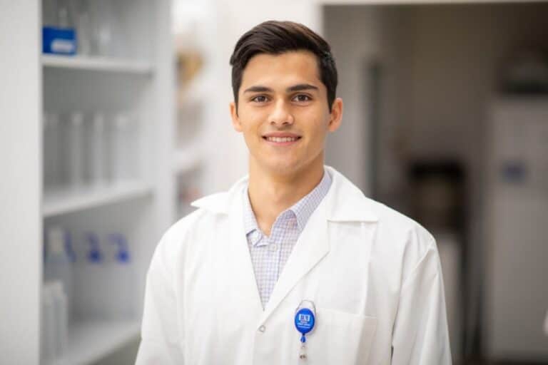 Nathan Bliss is dressed in a white lab coat standing in a research facility.