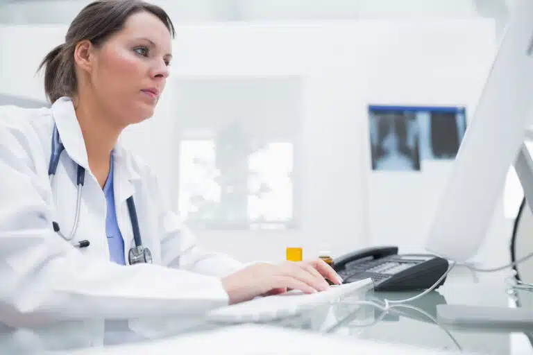 Side view of young female doctor using computer at clinic