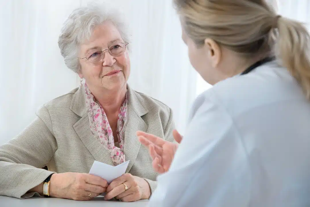 An elderly woman speaks with her doctor, who is explaining the prescription.