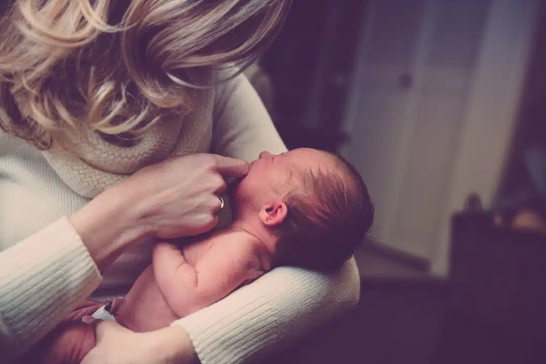 A blond woman cradles her infant in her arms, trying to soothe them.