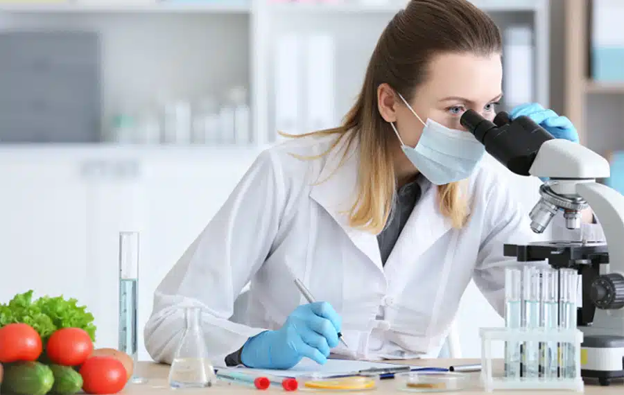 Person wearing a lab coat and looking into a microscope in a lab setting