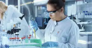 A scientist in a lab coat carefully pipettes liquid into a test tube in a laboratory setting, focused on research aimed at curing epilepsy.