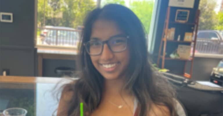 An individual smiling and holding a drink in a coffee shop setting.