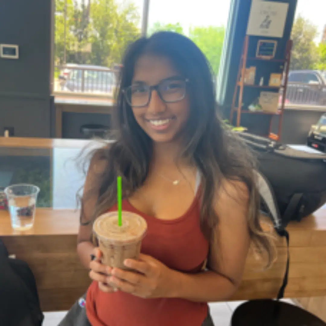 An individual smiling and holding a drink in a coffee shop setting.