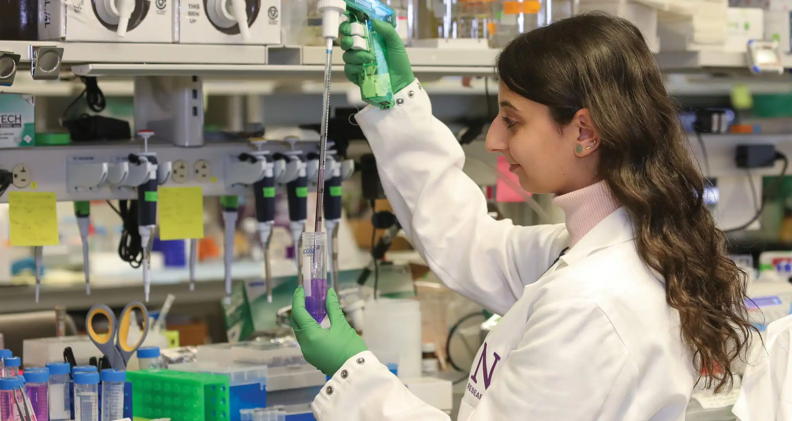 A scientist in a lab coat carefully pipettes liquid into a test tube in a laboratory setting, focused on research aimed at curing epilepsy.