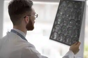 A doctor is holding up brain imaging up to a bright screen for patient results.