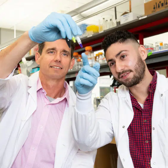 Two men in lab coats and medical gloves looking at lab equipment for research.