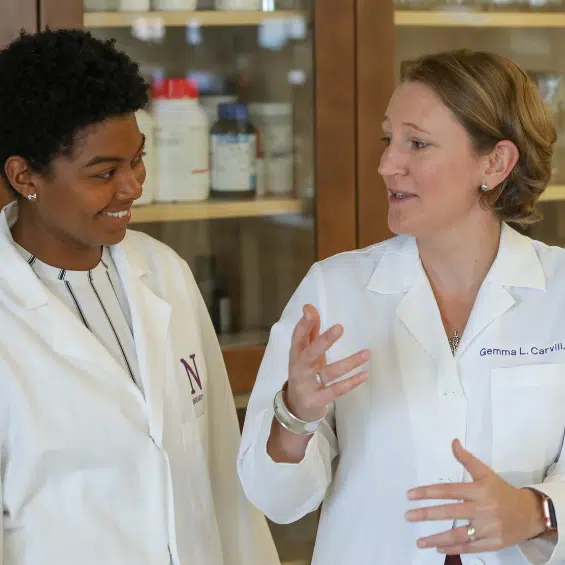 Two women in lab coats having a conversation, smiling.