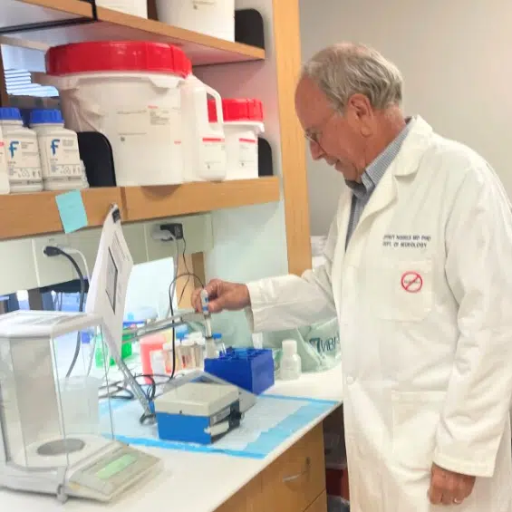 Man in lab coat using lab tools in brightly lit room.