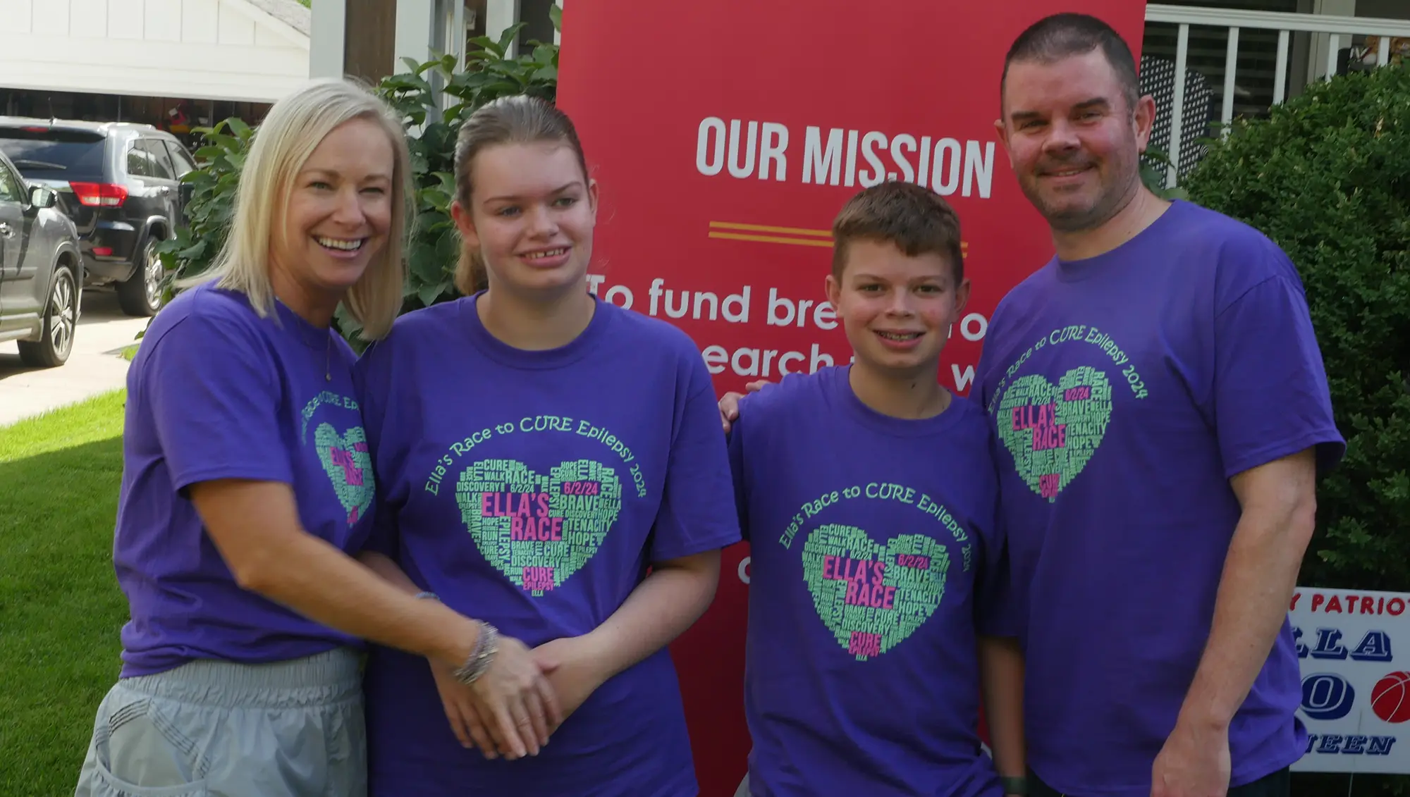 A family smiling at camera wearing Ella's race t-shirts in front of CURE Epilepsy mission statement.