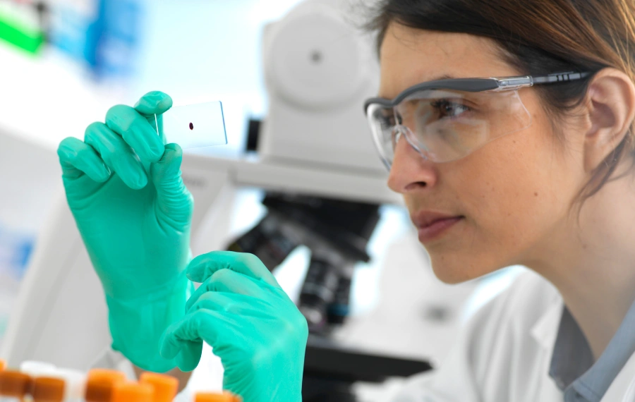 Researcher examines lab data wearing hospital gloves and safety goggles