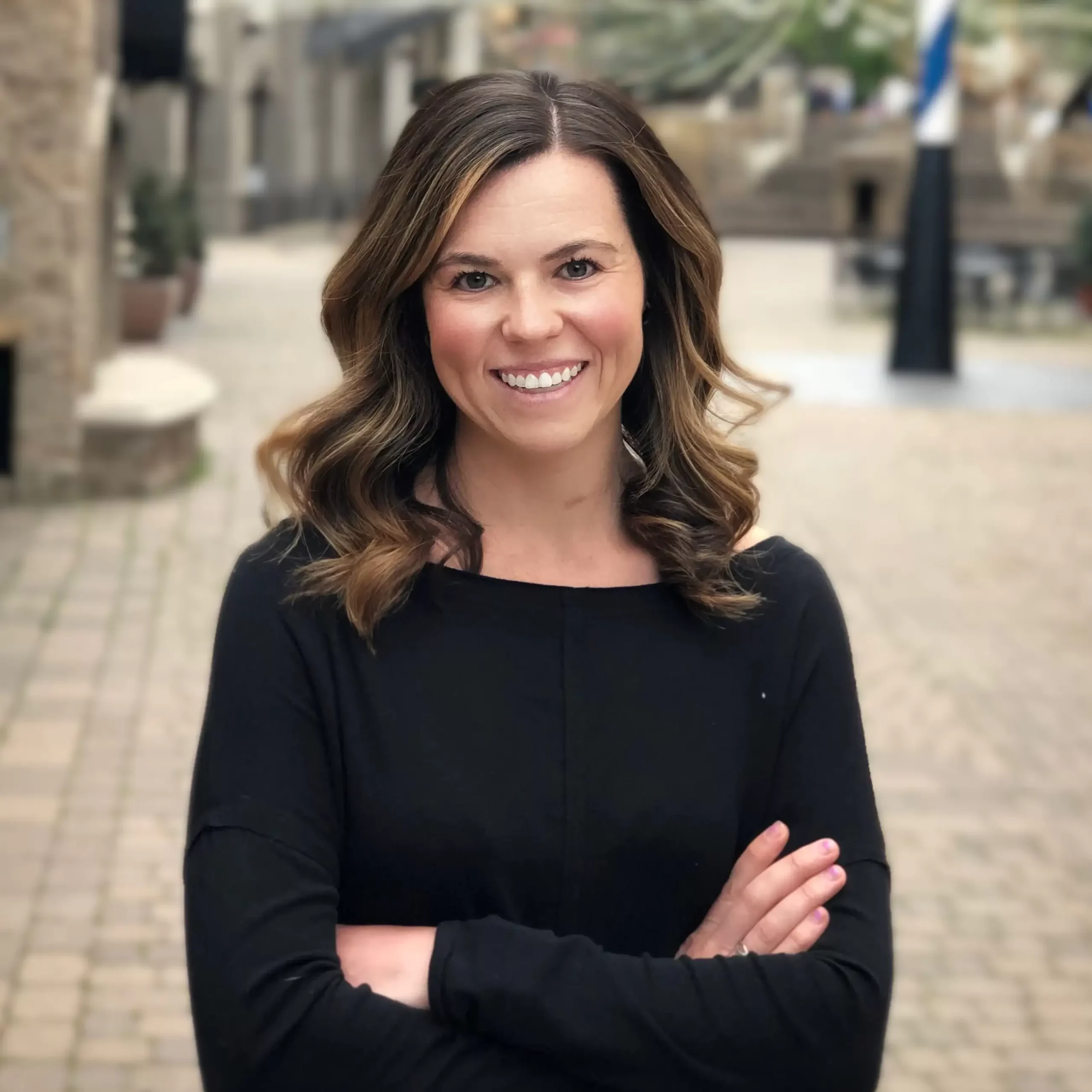 Photo of woman smiling at camera wearing black top with her arms crossed.