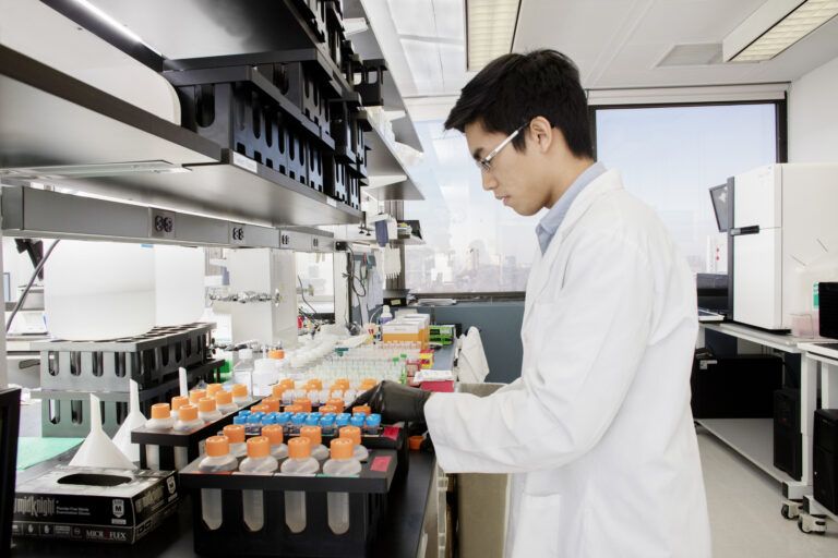 A young researcher wearing a white lab coat performing genetic testing on orange test tubes.