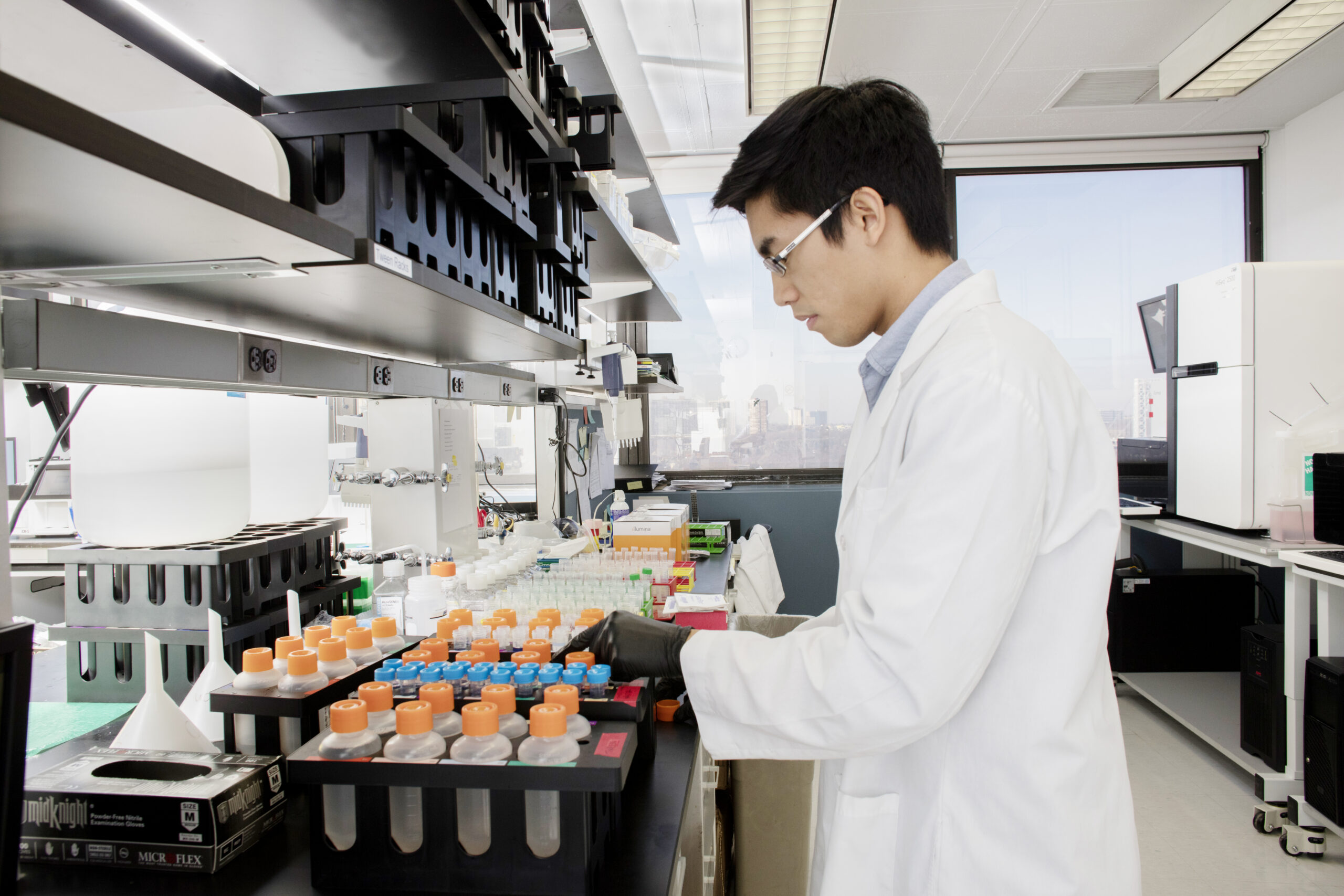 A young researcher wearing a white lab coat performing genetic testing on orange test tubes.