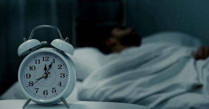 An alarm clock sits on a nightstand in a dark room while a person with epilepsy sleeps.