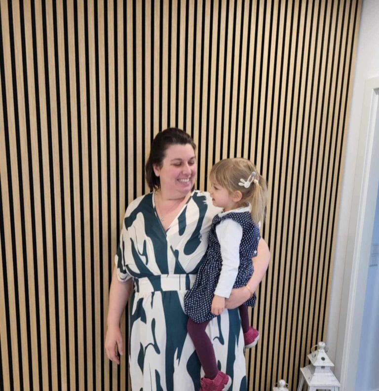 Cindy is holding little Anny. Both are dressed nicely and smiling at each other.