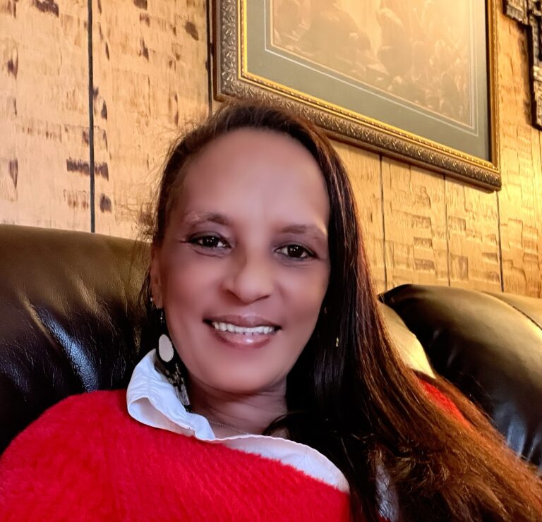 A woman is smiling at the camera wearing a red shirt.