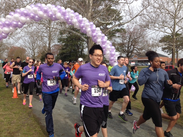 Runners wearing purple shirts cross the starting line at the annual 5K Strides for Epilepsy event.