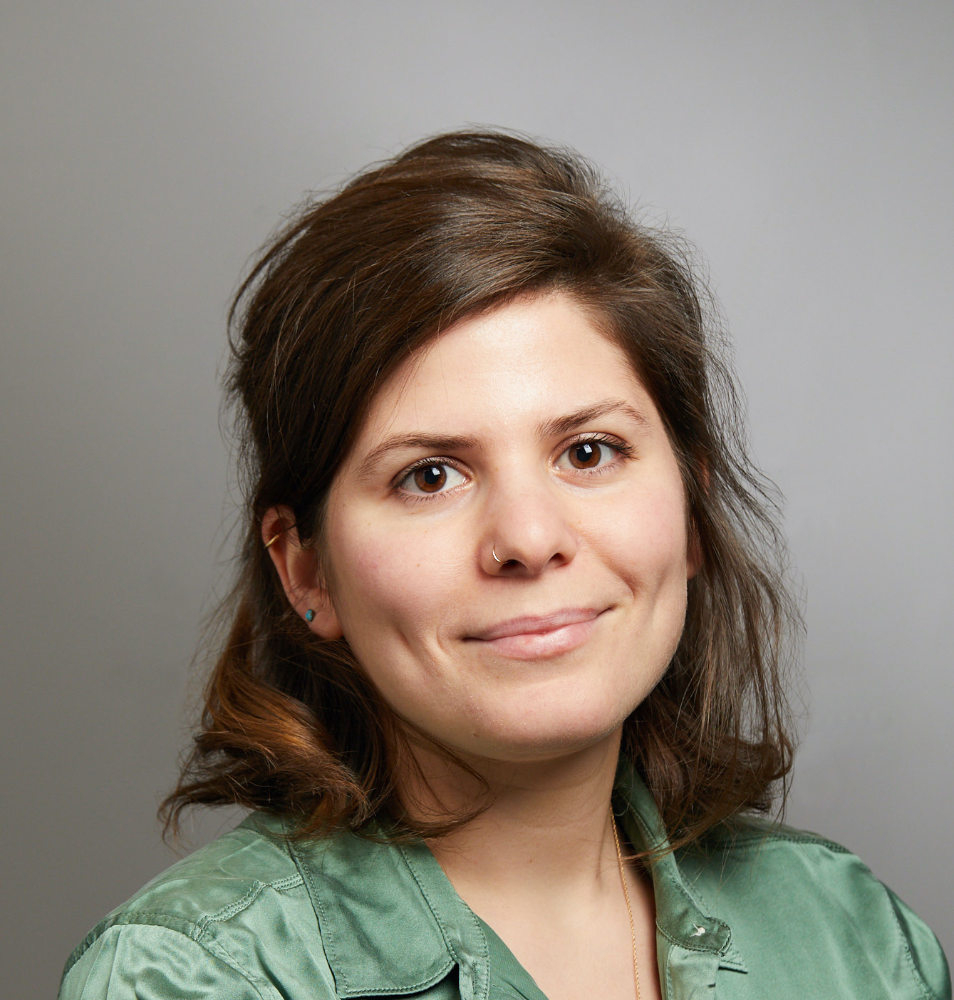 Woman with brown hair wearing a green top smiles for headshot in front of a gray background.