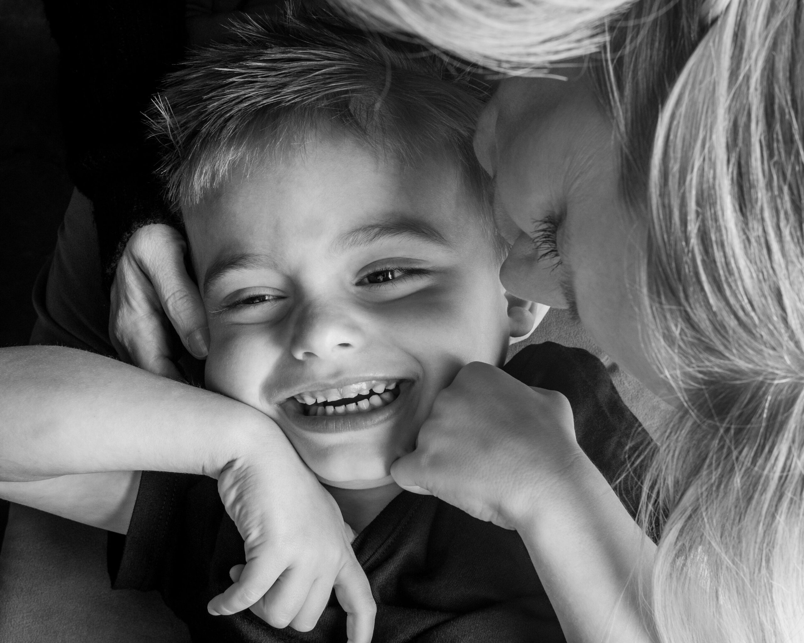 A close up photo of Max, a grade school kid, who is smiling while his mom, Amber, gives him a hug.