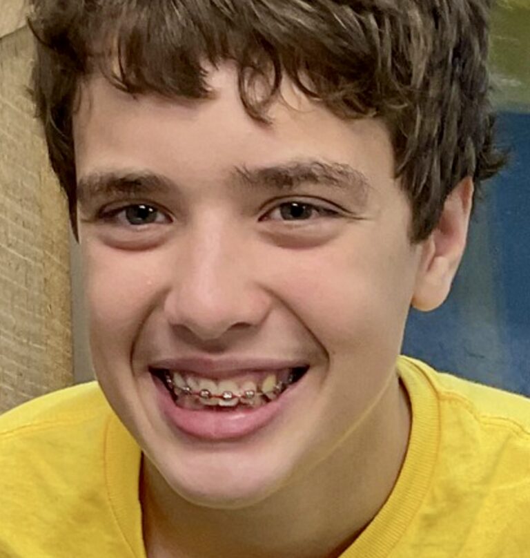 Photo of young man with dark hair smiling at the camera wearing a yellow t shirt.