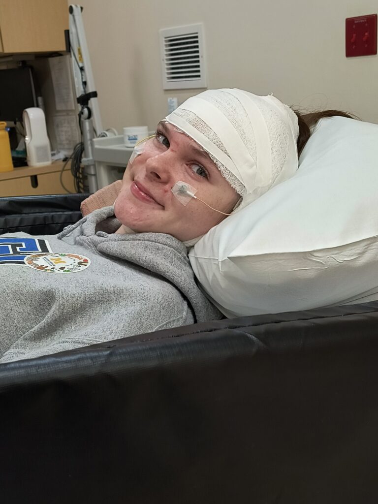 A young woman smiles for a photo wearing EEG wires in a hospital like setting.