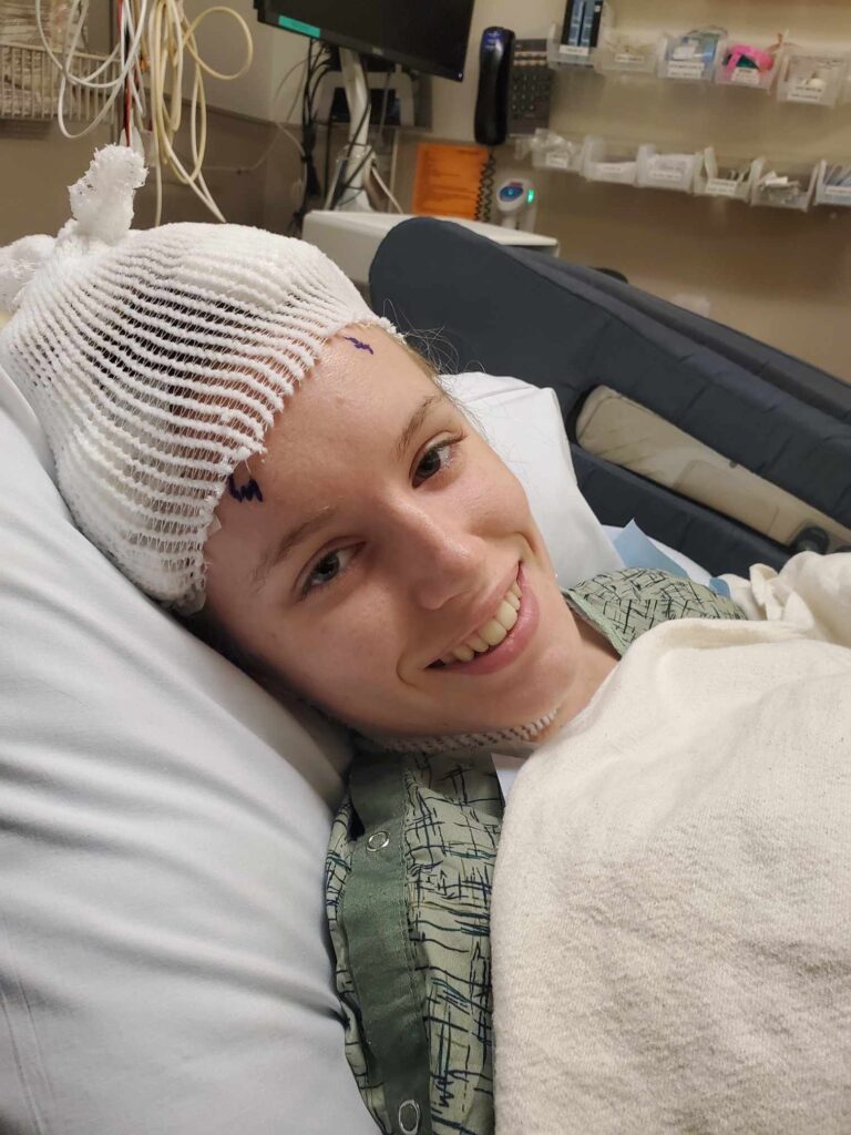 A young woman smiles wearing an EEG cap in a hospital bed.