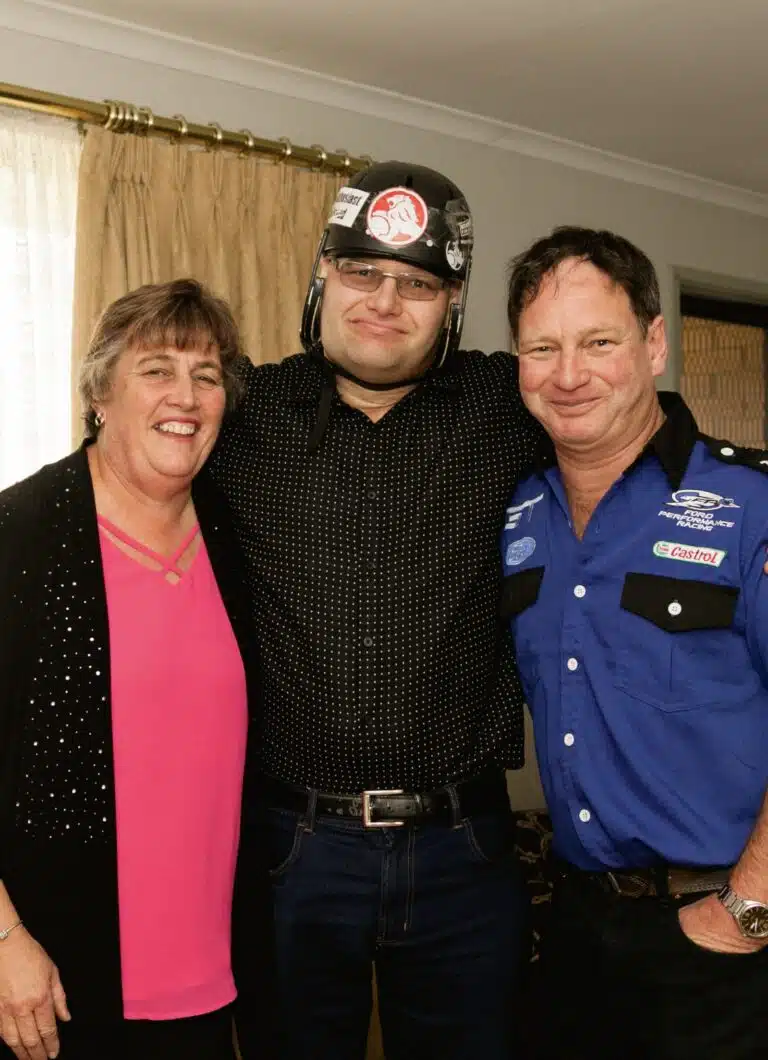 Three people posing for a photo, one is wearing a helmet for protection to his brain.