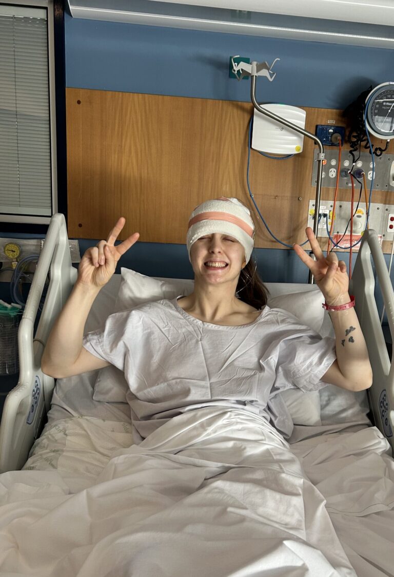 Woman with epilepsy laying in a hospital bed wearing an EEG cap holding up peace signs.