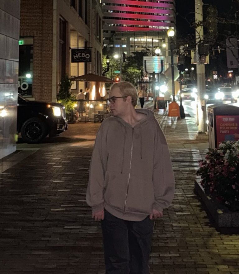A person stands center of frame in front of a cityscape.