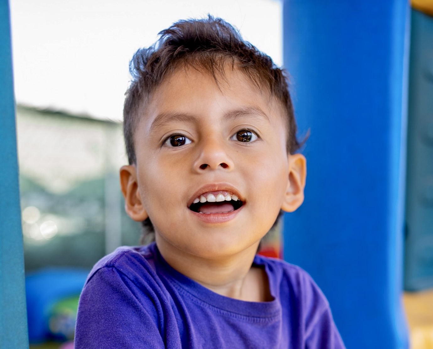 A young boy wearing purple shirt smiles at the camera.