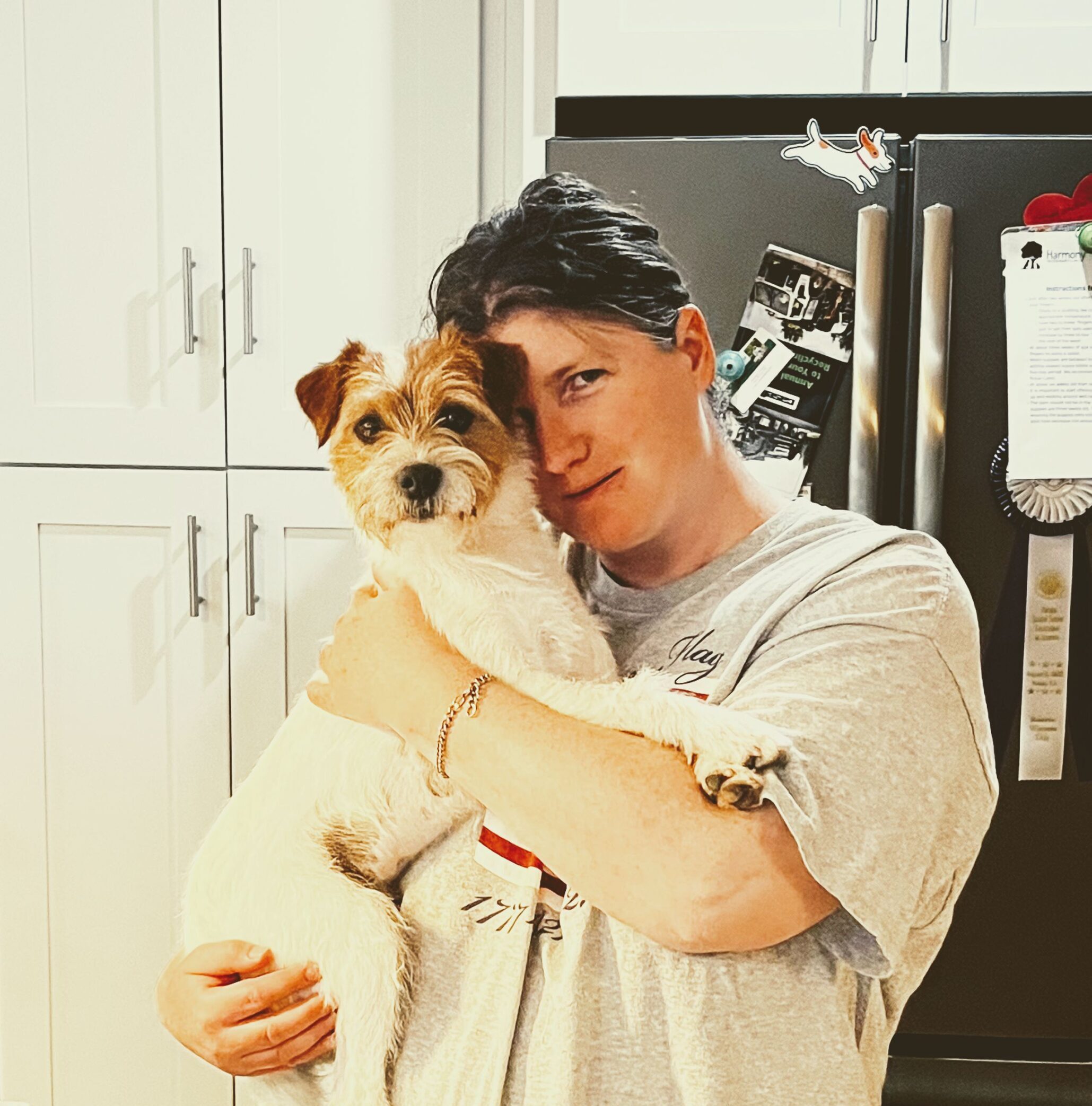 A person holds their dog inside indoors while looking into the camera.