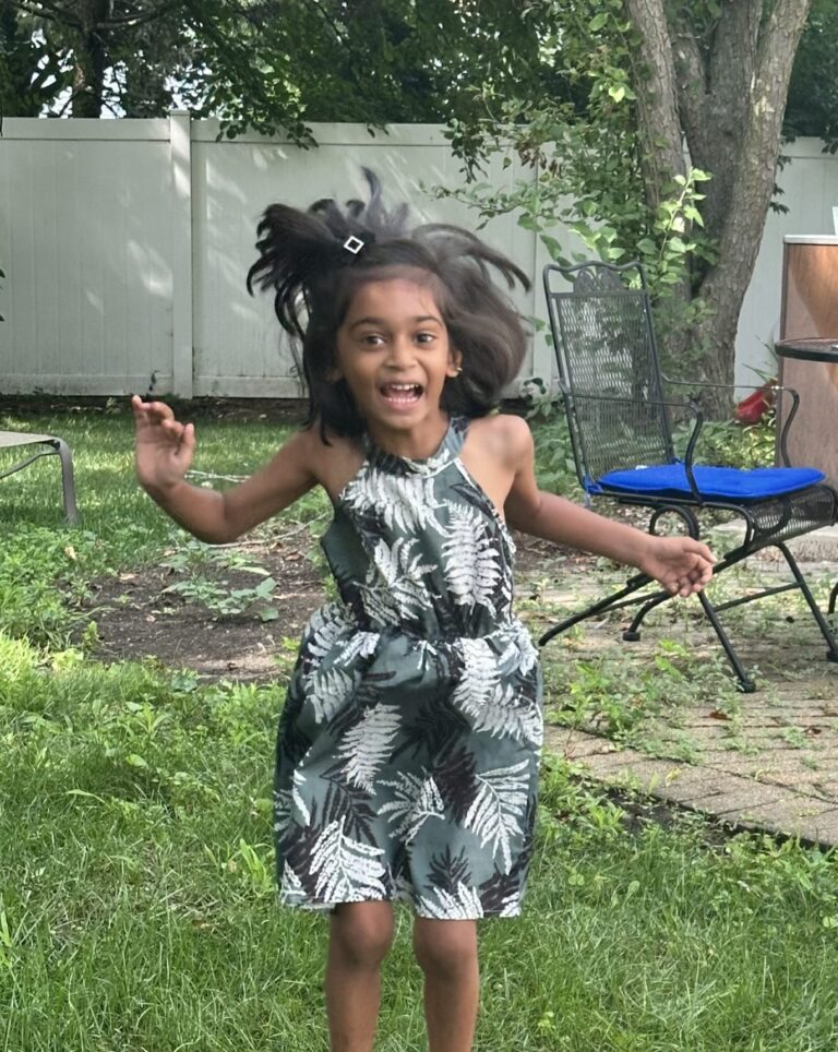 A child wearing black floral dress jumps joyfully outdoors.